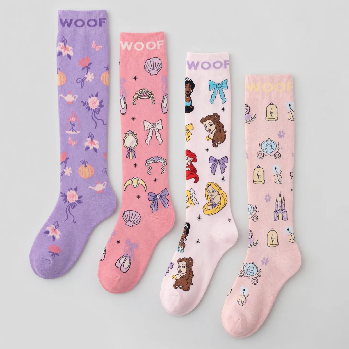 Flat lay display featuring four pairs of Disney Princess knee-high compression socks lined up side-by-side, including Magic Carriage & Lamp (lilac), Princess Icons (pink), Character Collage (light pink), and Cinderella (soft pink), all featuring "WOOF" top cuff branding.