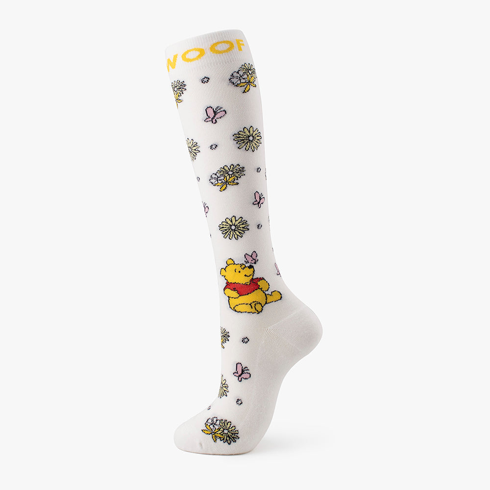 Studio shot of the off-white pair from the Disney’s Winnie the Pooh Bamboo Compression Socks 4 Pack, showcasing a yellow "WOOF" cuff band, scattered daisies, pink butterflies, and Winnie the Pooh character graphics.   