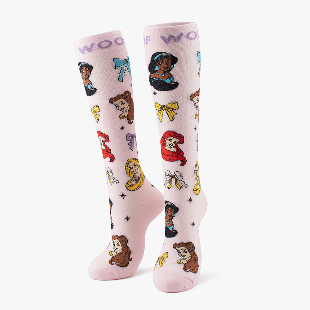 Side-by-side standing display of the light pink Disney Princess knee-high compression socks printed with character portraits and blue bows.
