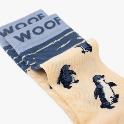 Folded view showing cute penguin illustration on cream bamboo crew compression socks with penguin design.